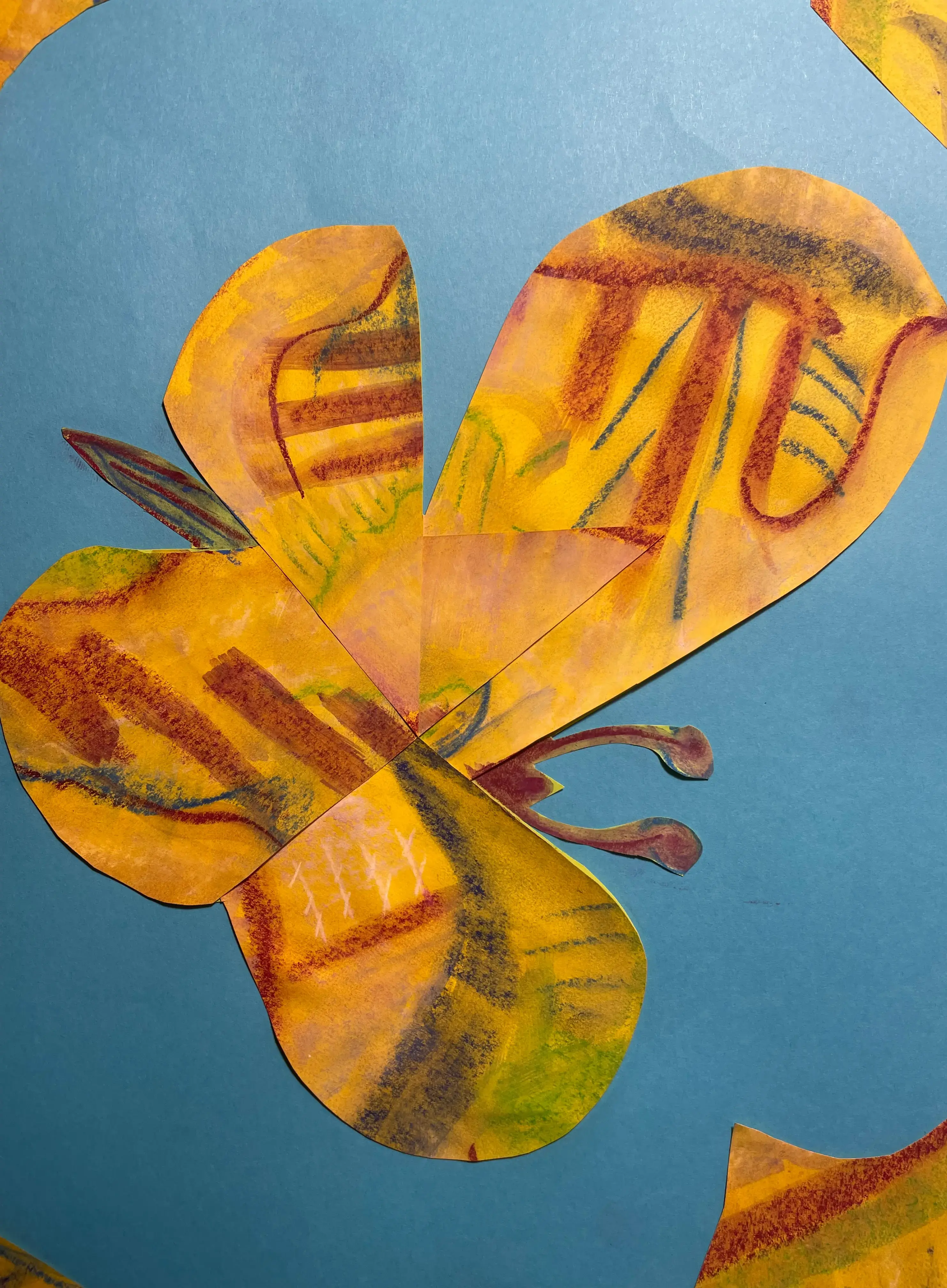Ein farbenfroher Schmetterling aus ausgeschnittenem Papier liegt vor blauem Hintergrund. Seine Flügel bestehen aus gelb-orangenen Formen, die mit roten, grünen und violetten Linien und Mustern bemalt sind, als trügen sie Spuren verschiedener Geschichten oder Gedanken. Die Collage wirkt handgemacht, lebendig und ein wenig fragmentarisch – als würde der Schmetterling aus unterschiedlichen Teilen zusammengesetzt, die nicht ganz zusammenpassen und gerade dadurch eine besondere, fragile Schönheit entfalten.